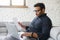 Mixed-race indian man in casual shirt sits on the couch and doing paperwork