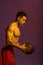 Mixed race man with muscular torso holding brown ball on purple background