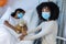 Mixed race mother and sick daughter in face masks in hospital, girl sleeping and holding teddy bear