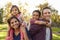 Mixed race parents carry their kids piggyback in a park