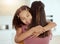 Mixed race single mother and daughter hugging in living room at home. Smiling hispanic girl embracing single parent and