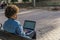 Mixed race woman with afro hair wearing blue denim shirt works with her laptop sitting on the bench of a park