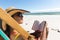 Mixed race woman on beach holiday sitting in deckchair reading book