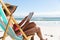 Mixed race woman on beach holiday sitting in deckchair reading book