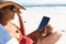 Mixed race woman on beach holiday sitting in deckchair using tablet