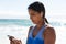 Mixed race woman exercising on beach wearing wireless earphones using smartphone