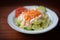 Mixed salad with carrot strips, tomato, lettuce and an industrial convenience dressing on a brown table