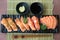 Mixed salmon sushi on black plate along with Japanese sauce and