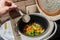 Mixed set of vegetarian vegetables in a white multicooker is stirred with a kitchen plastic scraper. Onions, peppers,