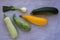 Mixed yellow, white, stripped and green zucchini`s and onion on a grey concrete background