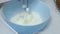 Mixer whisks whipping milk cream in blue bowl on white kitchen table, close up shot. Homemade food, baking sweet pastry, dessert