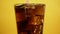Mixing cola cocktail with drinking straw. Sparkling soda on yellow background
