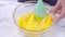 Mixing egg yolk into Chiffon cake batter with green silicone spatula mixer tool stirring until smooth and blend well in a glass bo