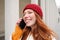 Mobile broadband and people. Smiling young redhead woman walks in town and talks on mobile phone, calling friend on