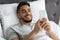 Mobile Gaming. Cheerful Young Arab Man Using Smartphone While Lying In Bed
