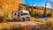 A mobile home stands next to a mountain road in bright autumn. Autumn vacation in a camper