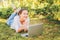 Mobile Office. Freelance business concept. Young woman lying on green grass lawn in city park working on laptop pc computer.