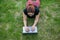 Mobile office. Top view of a freelancer woman typing a laptop while lying on the lawn. Work outdoors. Girl studying on a