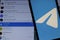 Mobile phone with Telegram Messenger logo on screen close up with Telegram app on laptop. Blurred background with free space.