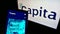 Mobile phone with website of British process outsourcing company Capita plc on screen in front of business logo.