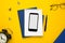Mobile phone with white notepad , blue notebook and pen on yellow background