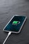 Mobile smart phone on wireless charging device on dark background. Icon battery and charging progress lighting on screen.