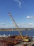 A Mobile Yellow Crane on the quayside of Alaskahaven, full of Piping, Concrete Ballast and Construction Materials