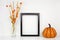 Mock up black frame with autumn branches and pumpkin decor on a shelf or desk