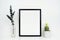 Mock up black frame with cactus and branches on a white shelf or desk against a white wall