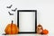 Mock up black frame with Halloween Jack o Lantern and pumpkin decor on a shelf against a white wall