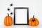 Mock up black frame with Halloween pumpkin decor on a shelf or desk against a white wall with spiders