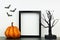 Mock up black frame with Halloween pumpkin and spooky tree decor on a shelf against a white wall