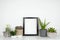 Mock up black portrait frame with cactus and succulent plants on a white shelf against a white wall