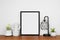 Mock up black portrait frame with home decor and potted plants on wood shelf against a white wall