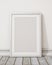 Mock up blank white picture frame on the white wall and the wooden floor, background