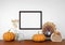 Mock up frame hanging from a white wall with thanksgiving turkey, pumpkin and autumn decor on a wood shelf