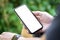 Mock up image of young man sitting in the park and holding smart phone with bank screen for advertisement