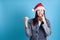 mock up of pensive surprised discouraged Asian young woman in Santa hat point to empty space isolated on blue background