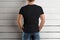 Mockup of a black t-shirt on a strong man holding his hands in the front pocket of jeans on a wooden background.