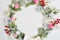 Mockup of Christmas Wreath Made of Naturalistic Looking Pine Branches Decorated with Red Berries and roses. Flat lay on a white wo