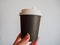 Mockup of female hand holding a coffee paper takeaway cup on grey background with copy space