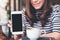 Mockup image of a beautiful woman holding and showing white mobile phone with blank black screen with smiley face and coffee cup o