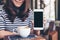 Mockup image of a beautiful woman holding and showing white mobile phone with blank black screen with smiley face and coffee cup o