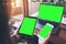 Mockup image of a businesswoman holding white mobile phone , black tablet and laptop with blank green screen on vintage wooden tab