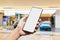 Mockup image of hand holding blank screen mobile smart phone with blurred background of new cars display in showroom, buying new