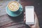 Mockup image of hand holding white mobile phone with blank screen with blue hot coffee cup on vintage wooden table