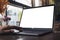 Mockup image of a hand using and touching laptop with blank white desktop screen and flower vase on wooden table