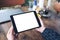 Mockup image of hands holding black tablet pc with blank desktop white screen and coffee cup on wooden table