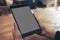 Mockup image of hands holding black tablet pc with gray blank screen on wooden table background