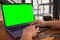 Mockup image of hands typing on laptop keyboard with blank green desktop screen and credit cards on wooden table
